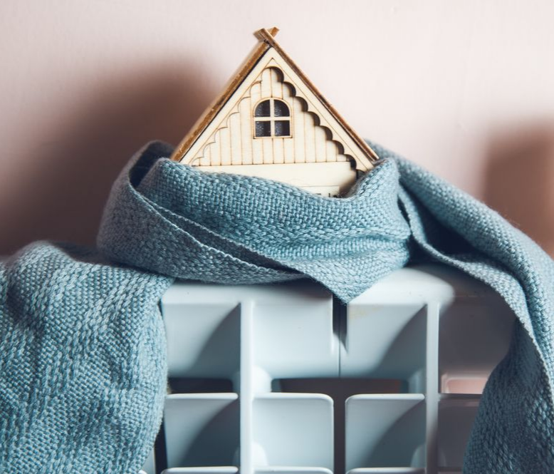 Petite figurine de maison enveloppée dans un foulard bleu, posée sur un radiateur.