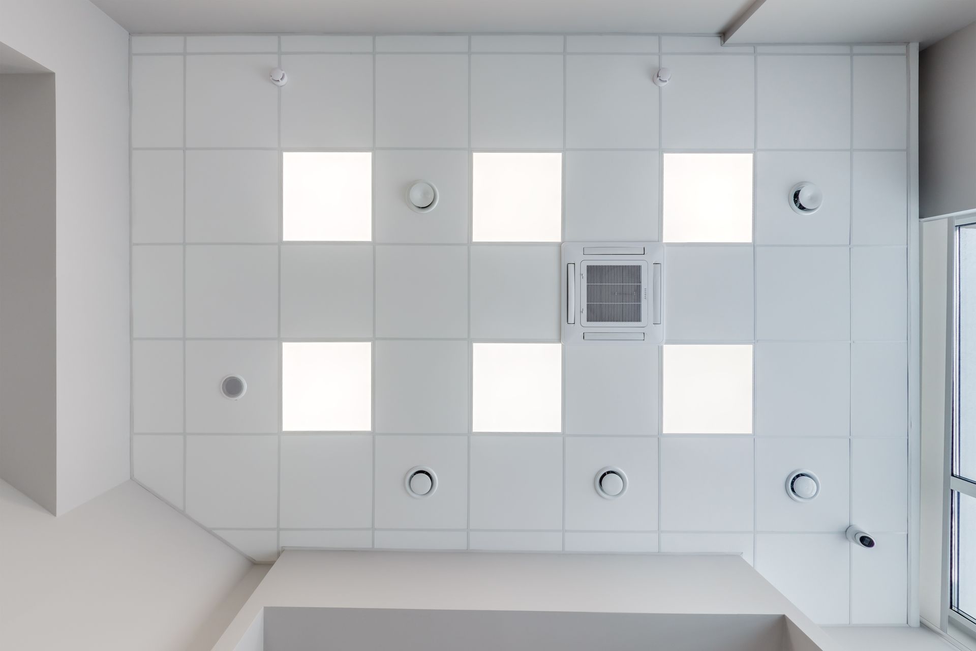 Un faux plafond en dalles avec des lumières et une unité de ventilation intégrées.