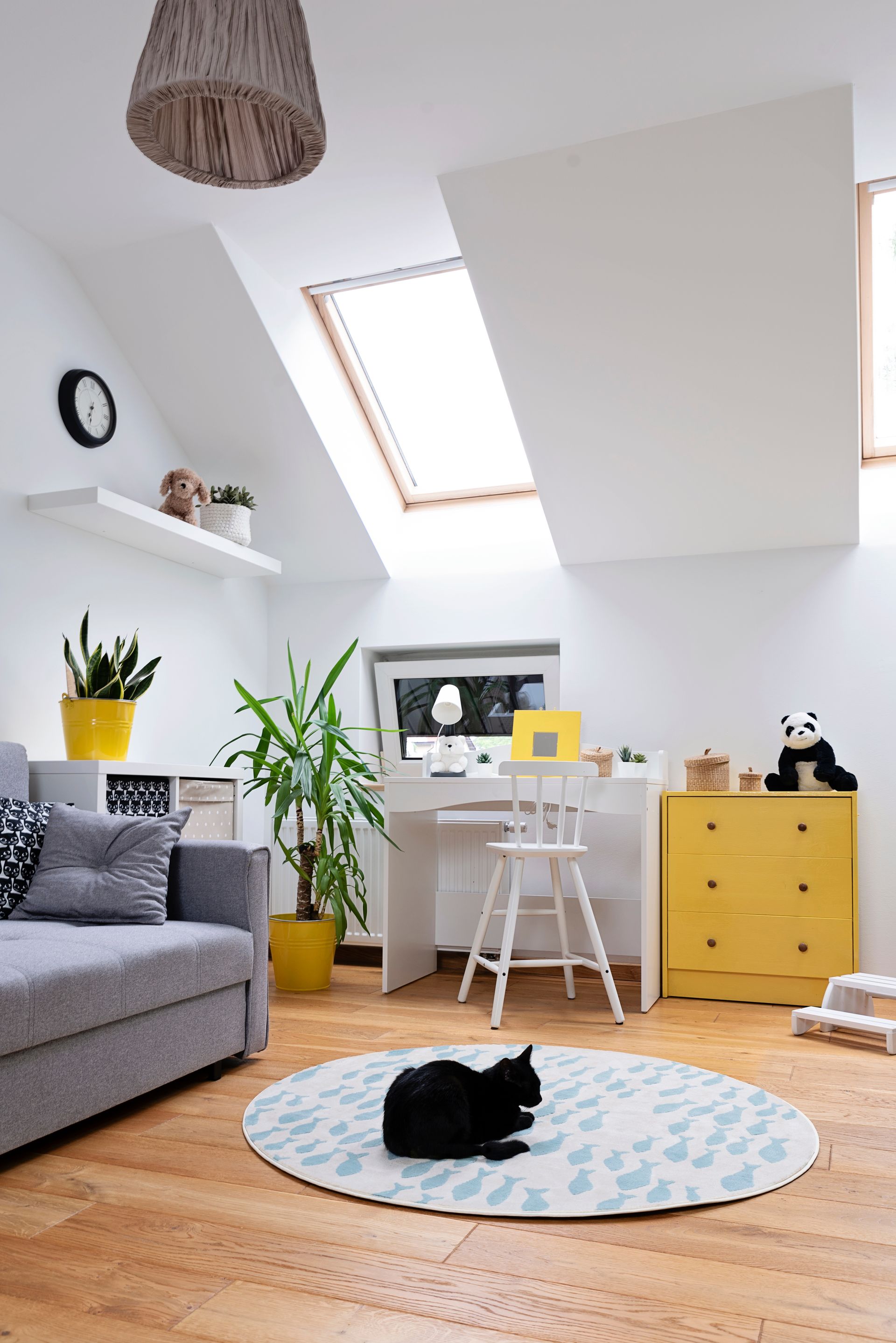 Une pièce mansardée lumineuse avec un canapé gris, un bureau et des plantes.