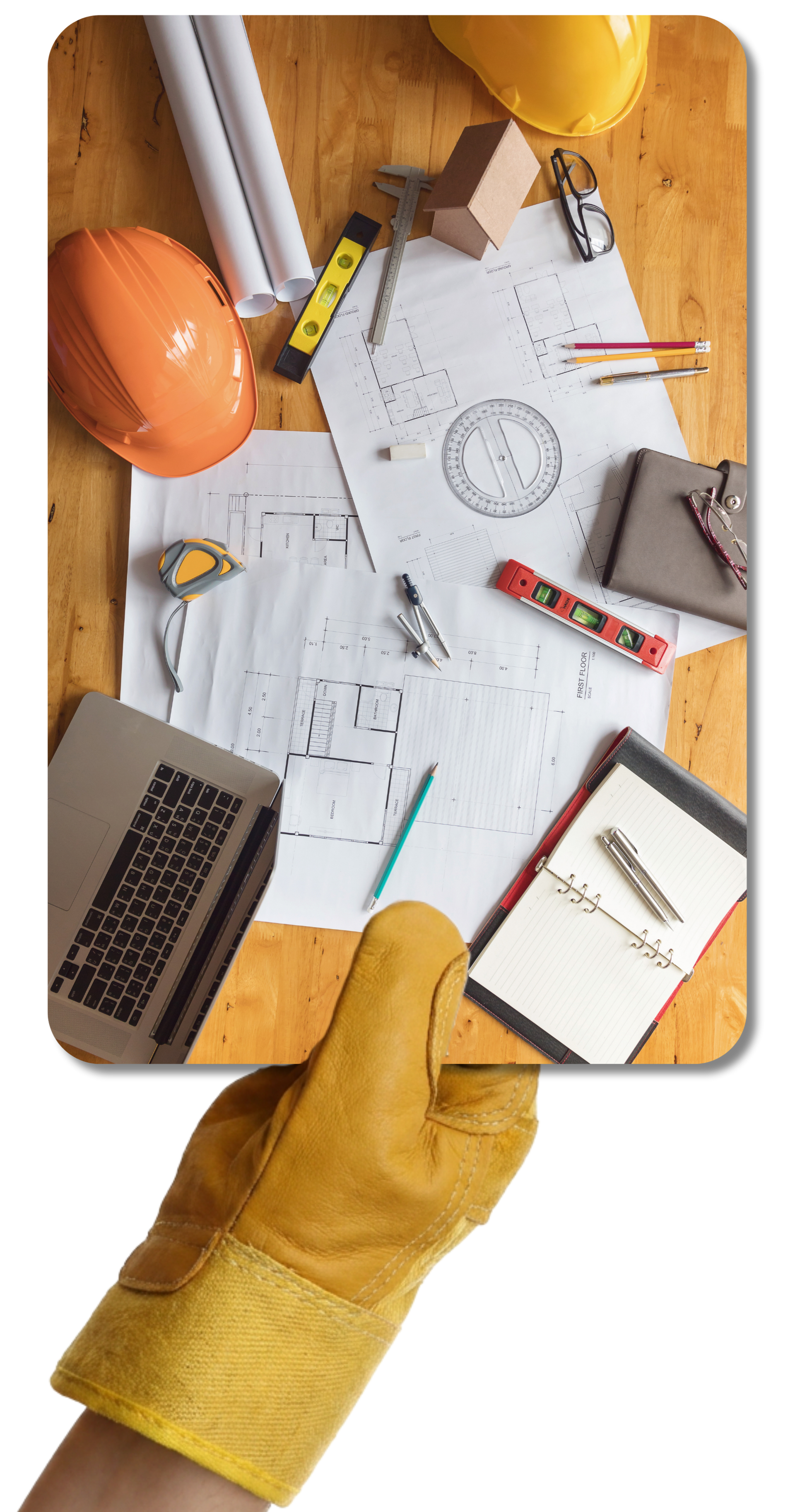 Une main gantée de jaune tient une image de plans de construction entourés de divers outils et accessoires.