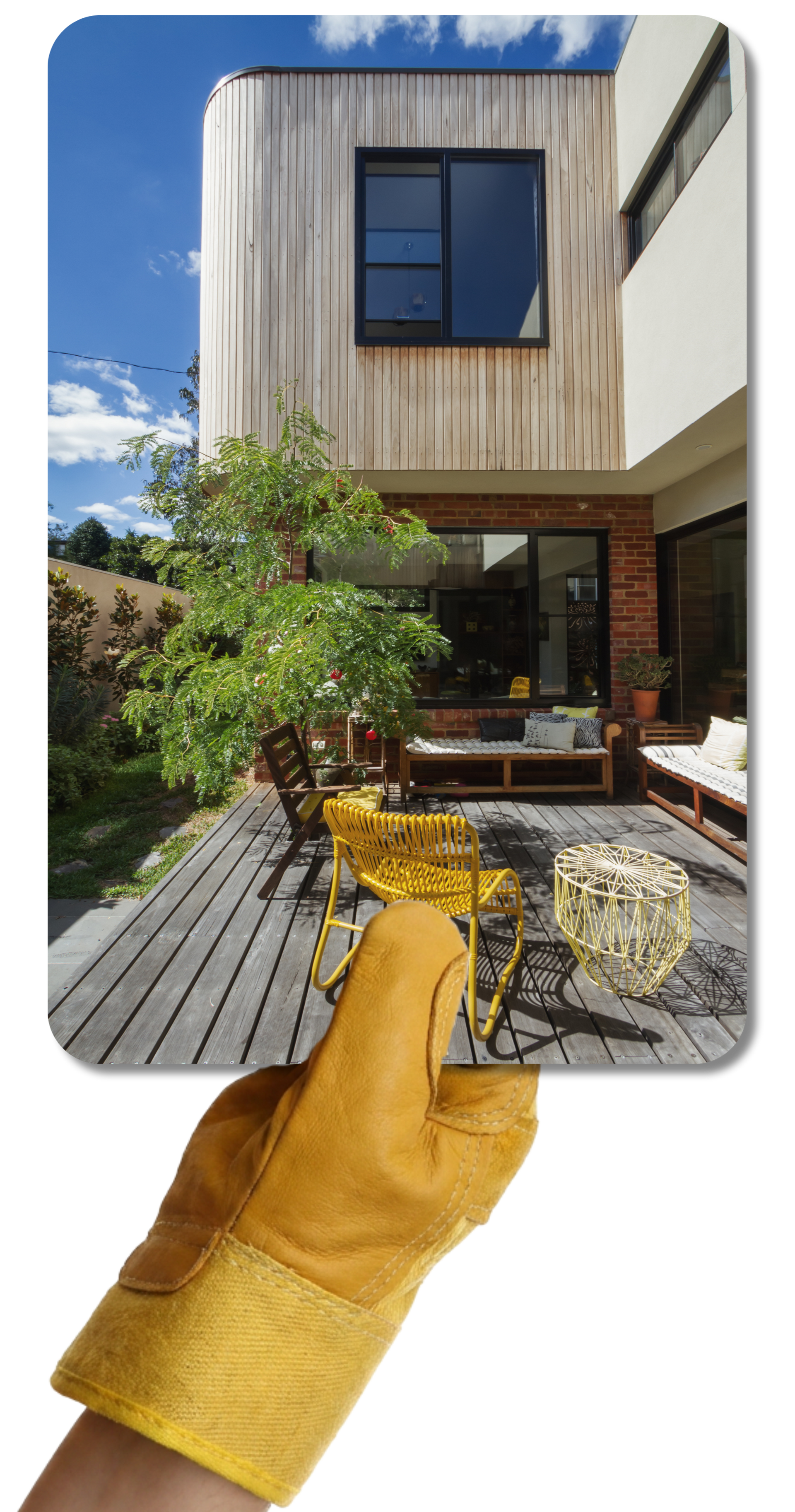 Une main gantée de jaune tient une photo d'une maison moderne avec une terrasse et une extension.