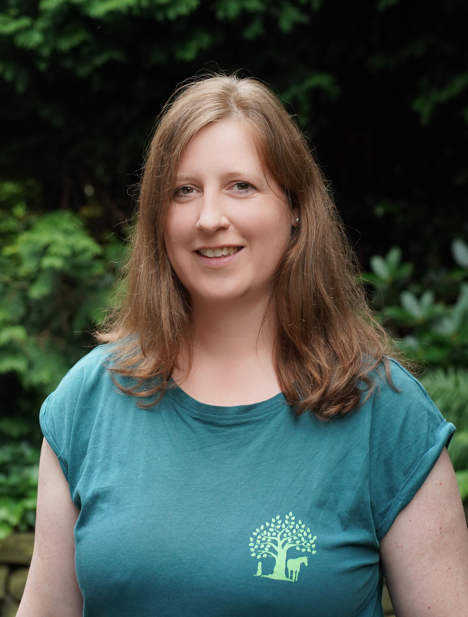 Eine Frau, die ein grünes T-Shirt mit einem Baum darauf trägt, lächelt in die Kamera.