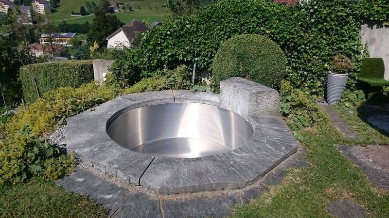 Ein Edelstahlbrunnen steht mitten in einem Garten. Foto von der Artmetal GmbH