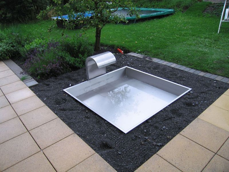 Ein Springbrunnen aus Edelstahl auf einer Terrasse neben einem Trampolin. Foto von der Artmetal GmbH