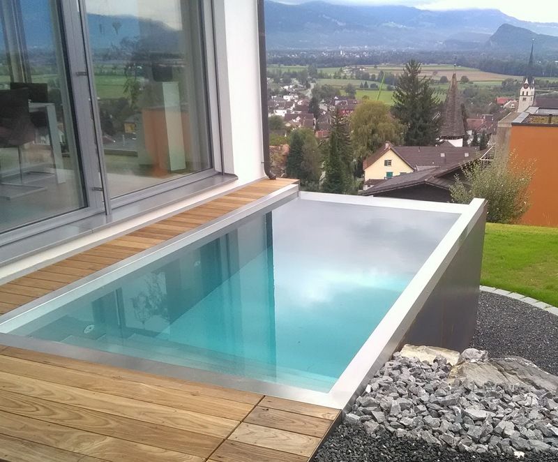 Auf einem Holzdeck neben einem Fenster steht ein kleiner Swimmingpool aus Edelstahl. Foto von der Artmetal GmbH