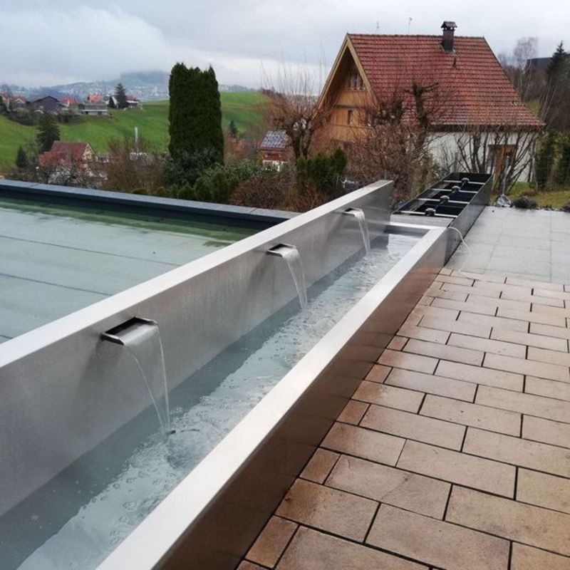 Ein Springbrunnen auf einem Ziegelweg mit einem Haus im Hintergrund. Foto von der Artmetal GmbH