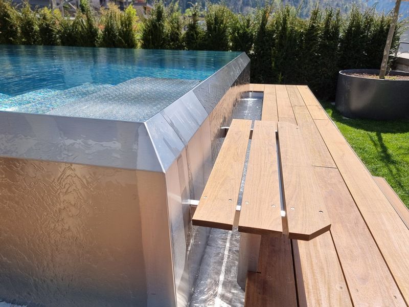 Eine Holzbank steht neben einem Swimmingpool aus Edelstahl. Foto von der Artmetal GmbH