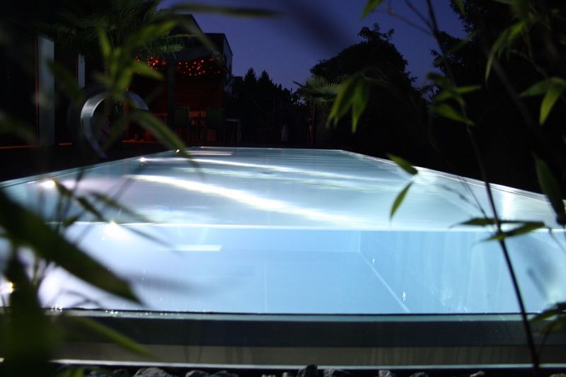 Ein Swimmingpool aus Edelstahl ist nachts beleuchtet und von Bäumen umgeben. Foto von der Artmetal GmbH