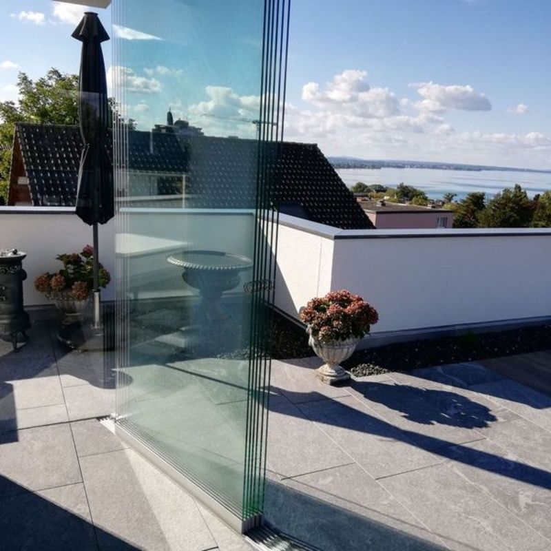 Eine Terrasse mit einer Glaswand und einer Vase mit Blumen. Foto von der Artmetal GmbH