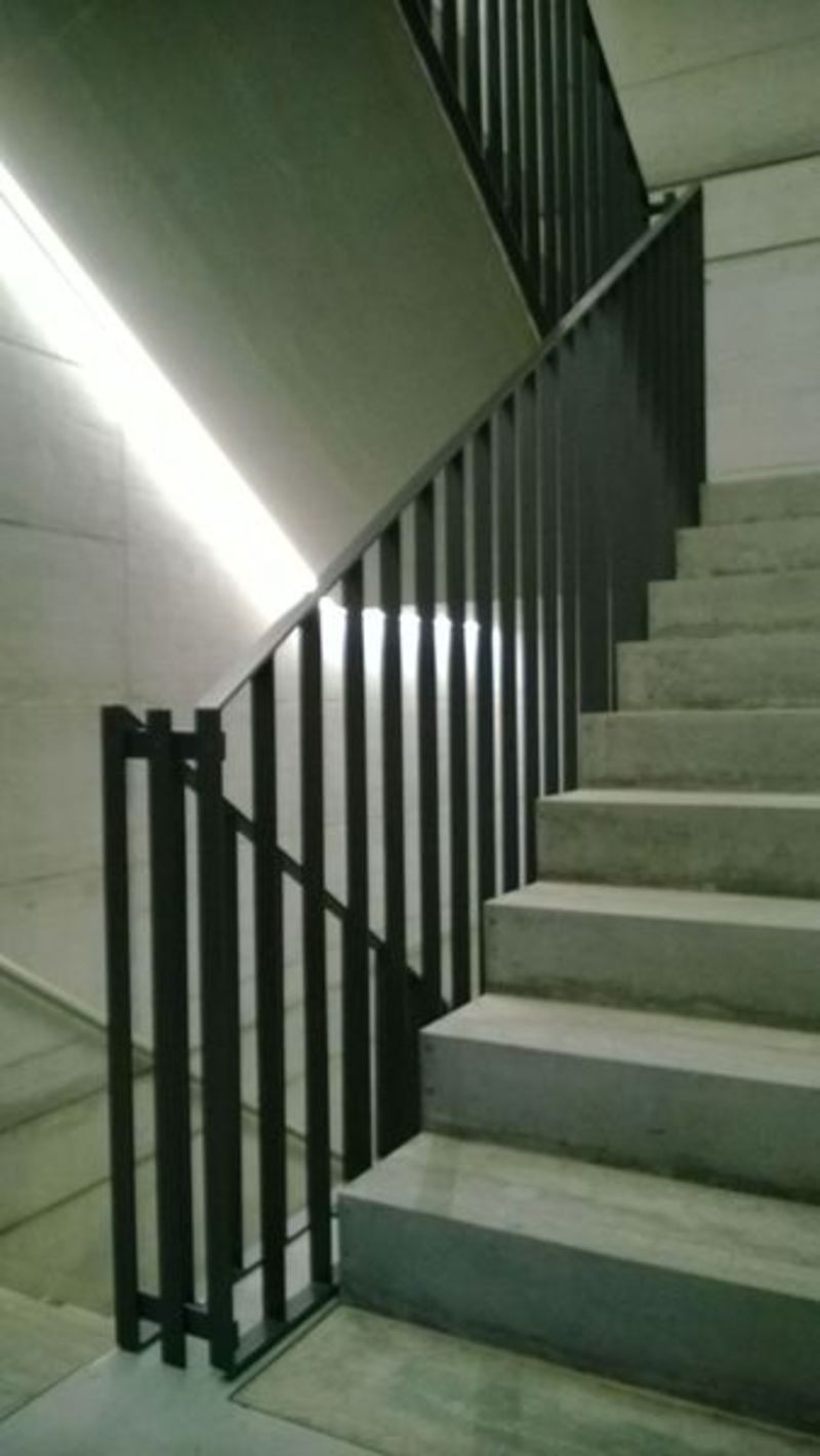 Eine Treppe mit einem schwarzen Geländer und einem Licht, das die Treppe herunterkommt. Foto von der Artmetal GmbH