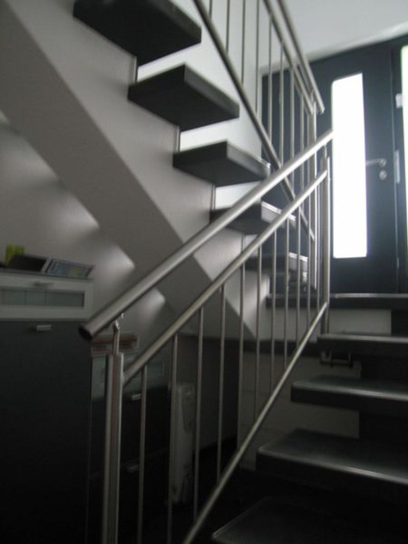 Eine Treppe mit Edelstahlgeländer und schwarzen Stufen. Foto von der Artmetal GmbH