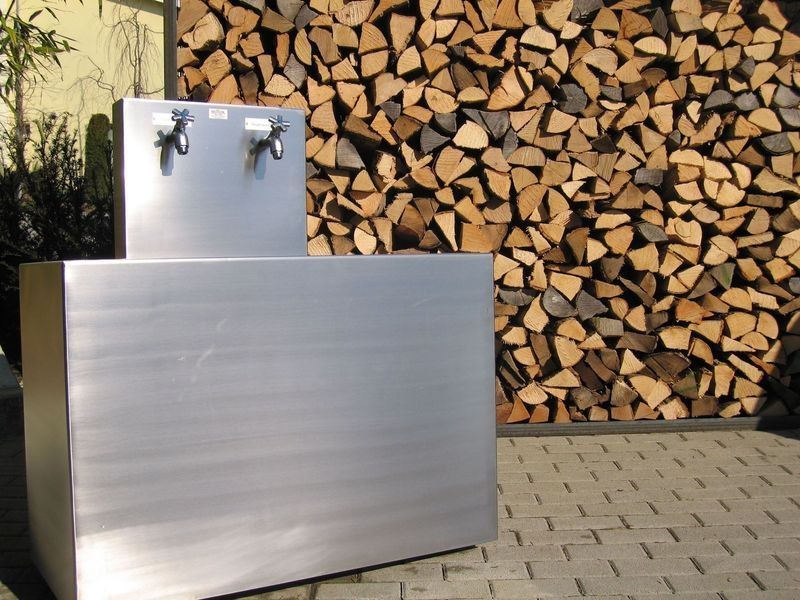 Eine Edelstahlspüle steht vor einem Stapel Holzstücke. Foto von der Artmetal GmbH