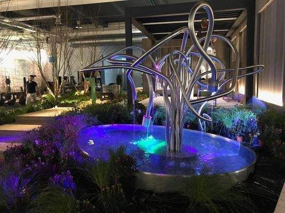 Ein Edelstahlbrunnen mit violetten Lichtern in einem Garten. Foto von der Artmetal GmbH