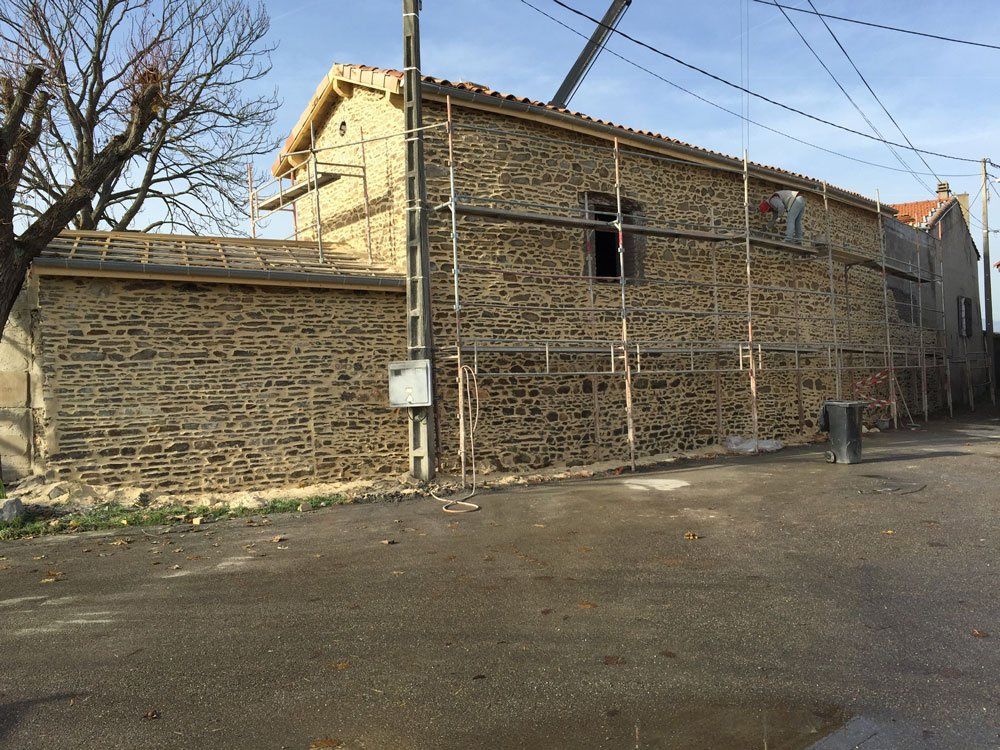 Grand mur de maison ancienne près d'une route avec un professionnel sur l'échafaudage