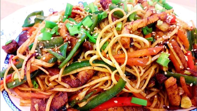 Fideos con verduras y carne, adornados con semillas de sésamo y cebollas verdes.