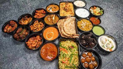 Surtido de platos indios en recipientes negros individuales, que incluyen curry, arroz, pan y postres, dispuestos sobre una superficie.