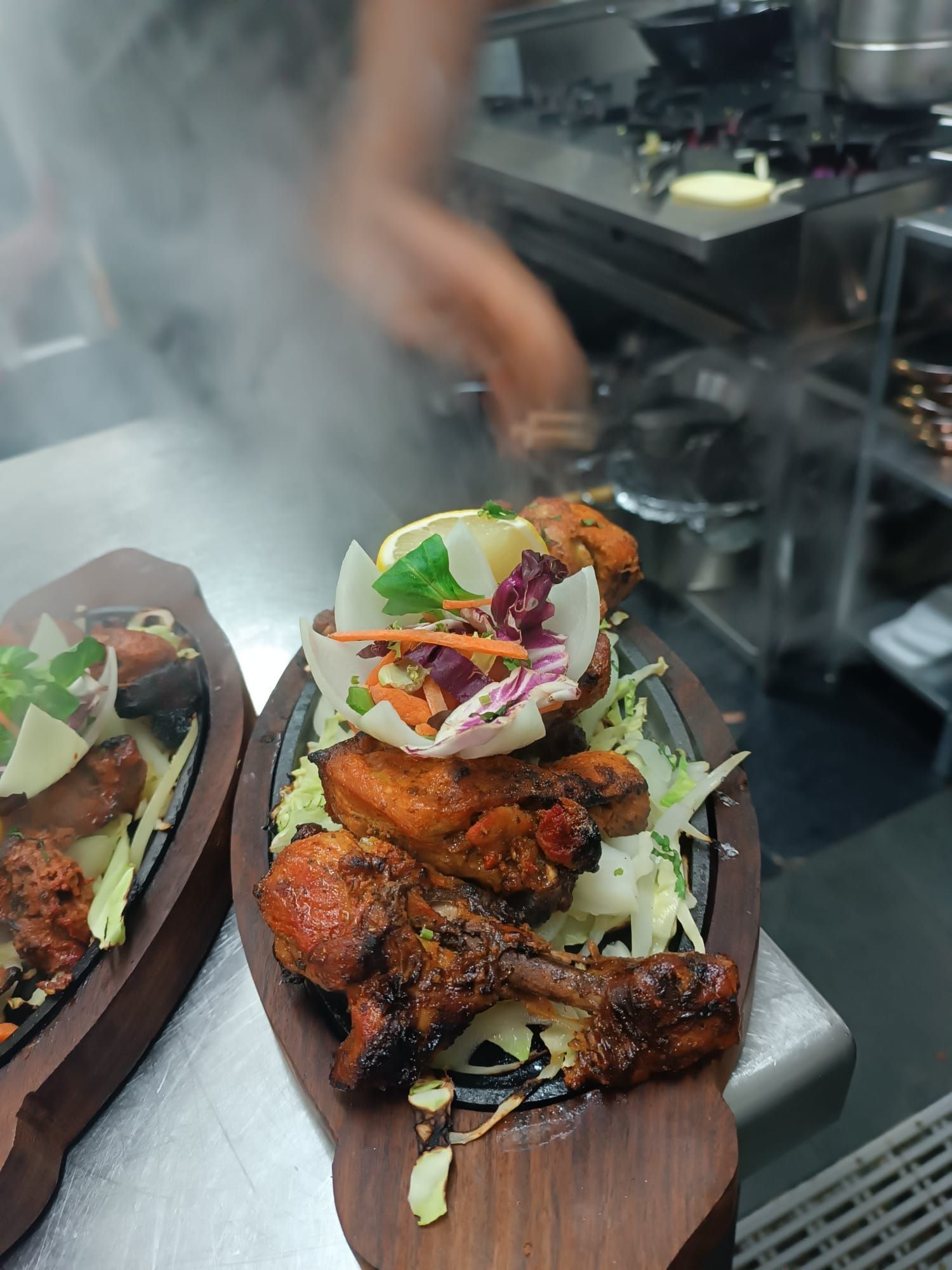 Pollo tandoori servido en una bandeja de madera con guarniciones, humeante en la cocina de un restaurante.