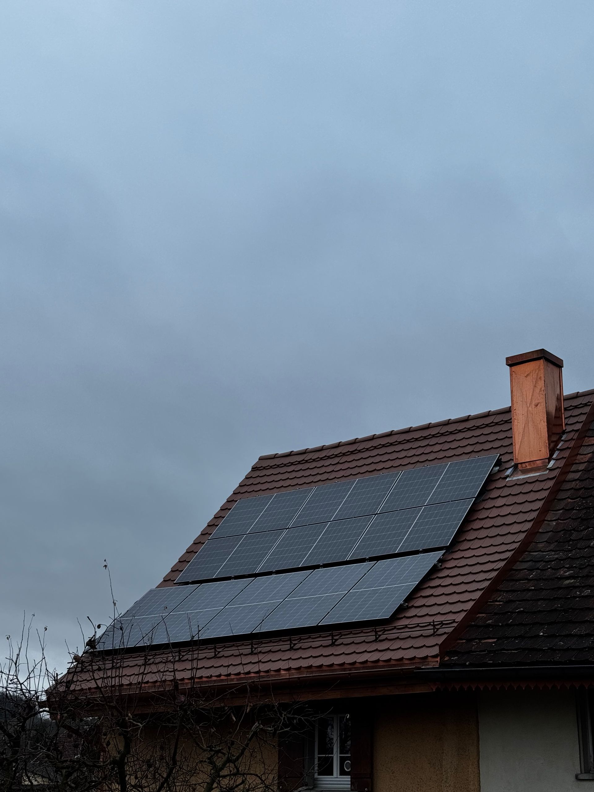 Solarpaneele auf einem rotziegelgedeckten Hausdach an einem bewölkten Tag.