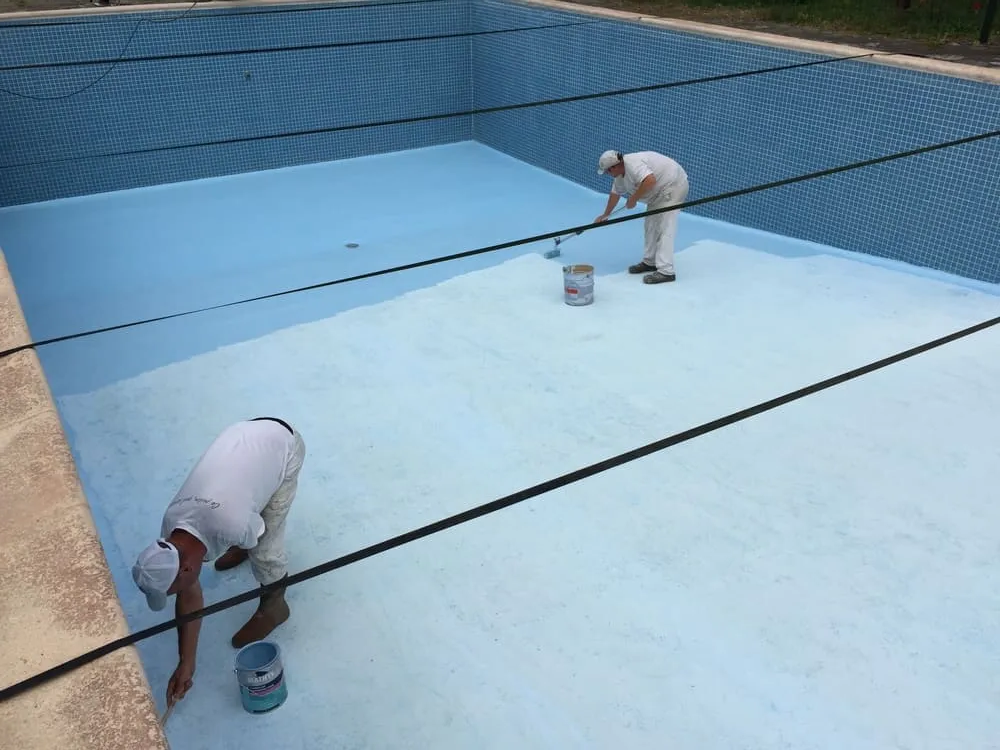 un homme peignant une piscine avec de la peinture bleue