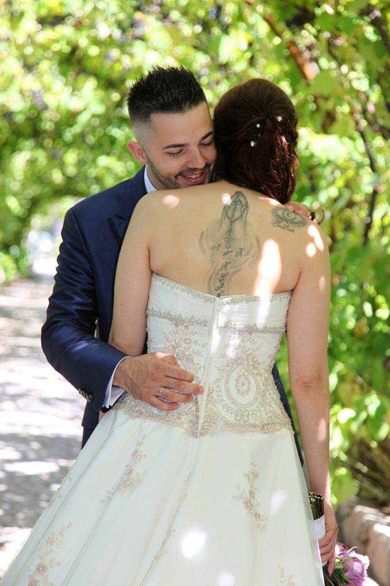 O noivo abraça a noiva por trás, sorrindo, em um jardim.