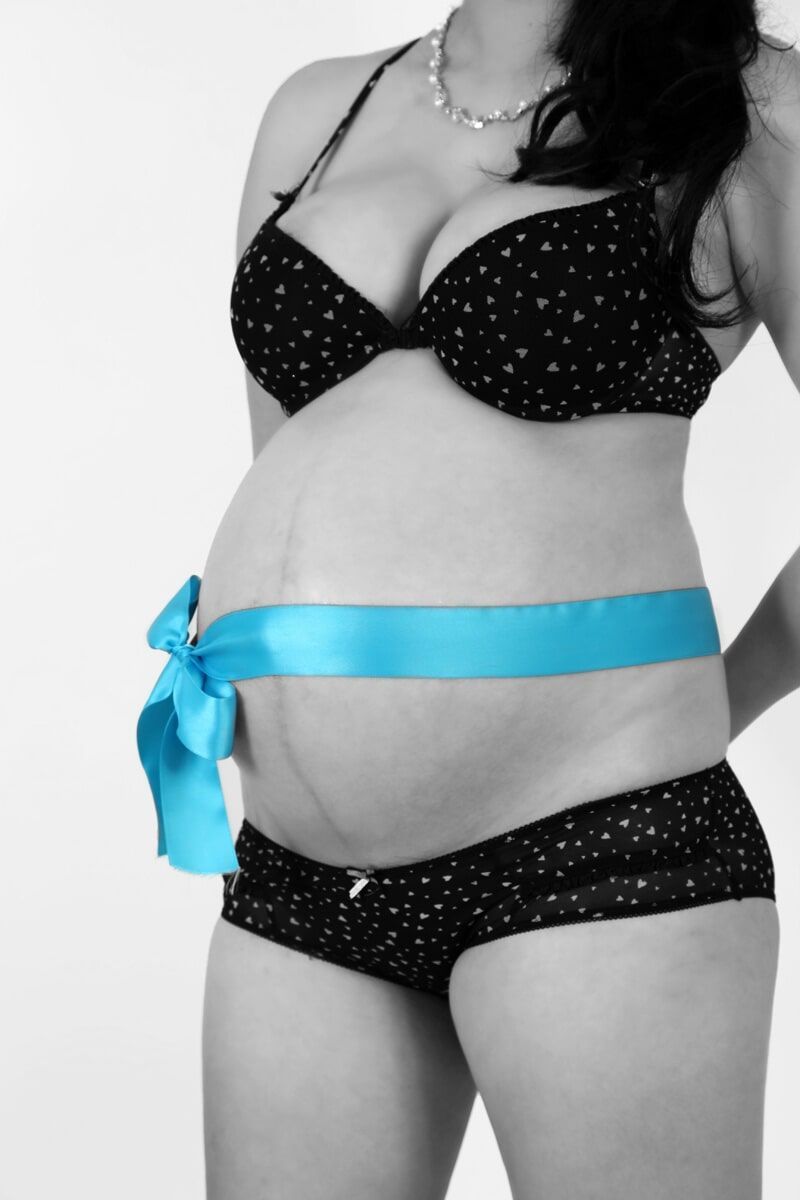 Mulher grávida vestindo lingerie de bolinhas, com uma fita azul amarrada na barriga.