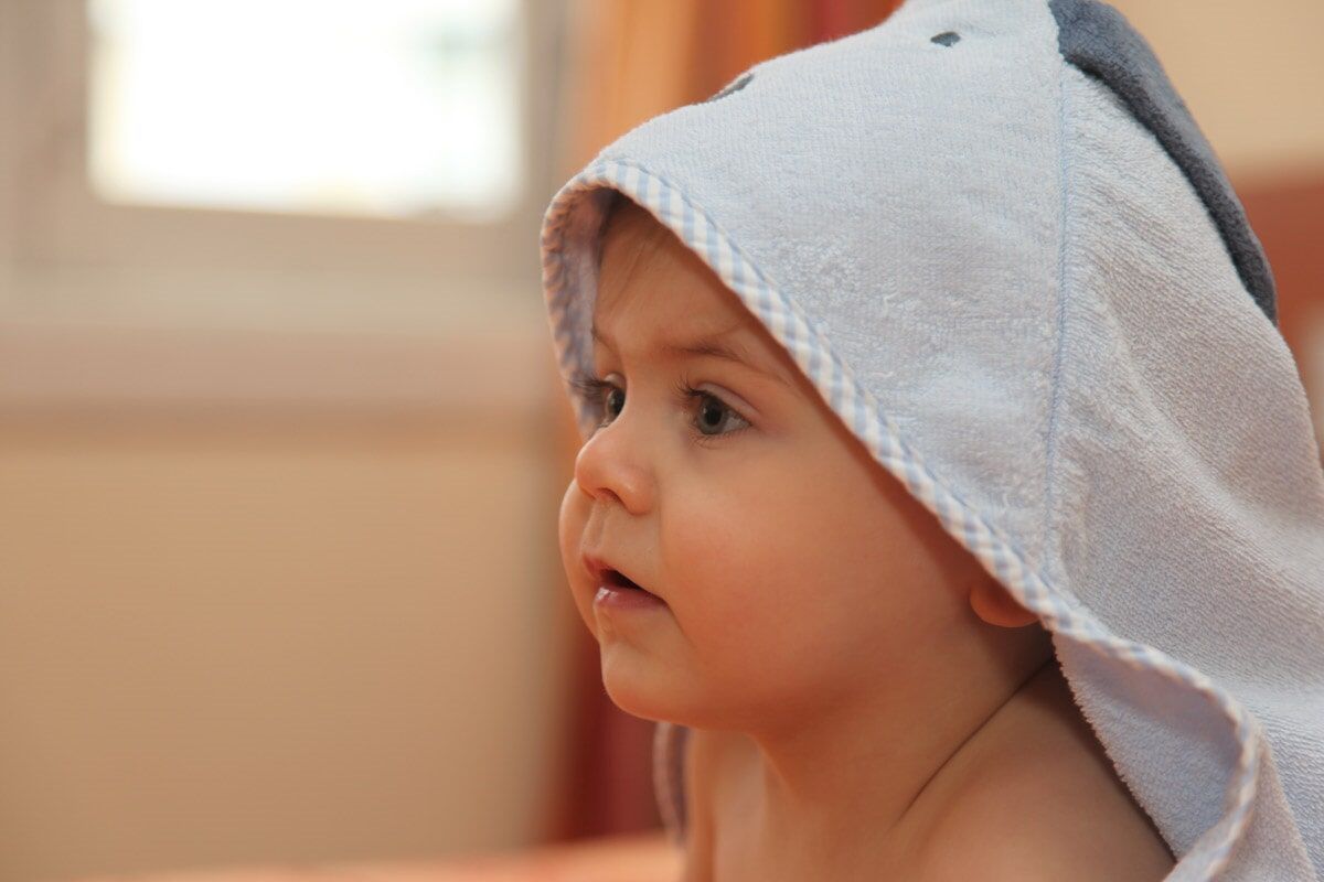 Bebê com toalha azul-clara com capuz, olhando para o lado, foco suave.