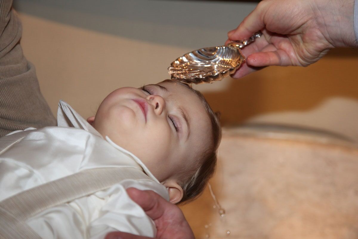 Bebê sendo batizado; água derramada sobre a cabeça com uma bacia de prata.