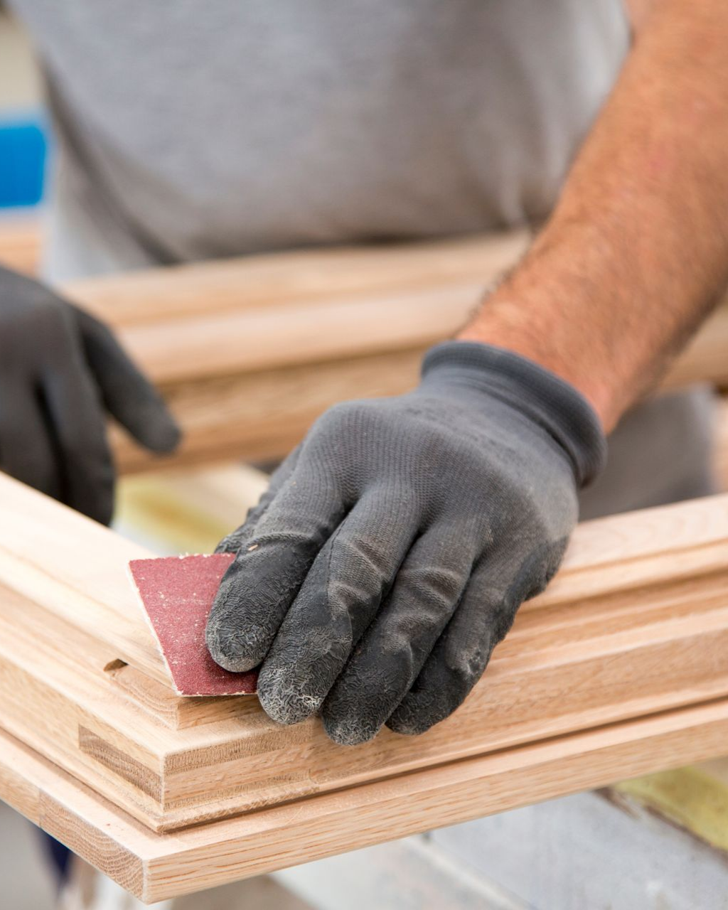 Personne ponçant un cadre en bois, portant des gants, à l'intérieur.