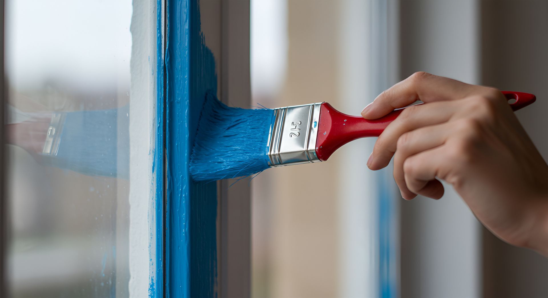 Peinture à la main de peinture bleue sur un cadre de fenêtre blanc avec un pinceau à manche rouge.