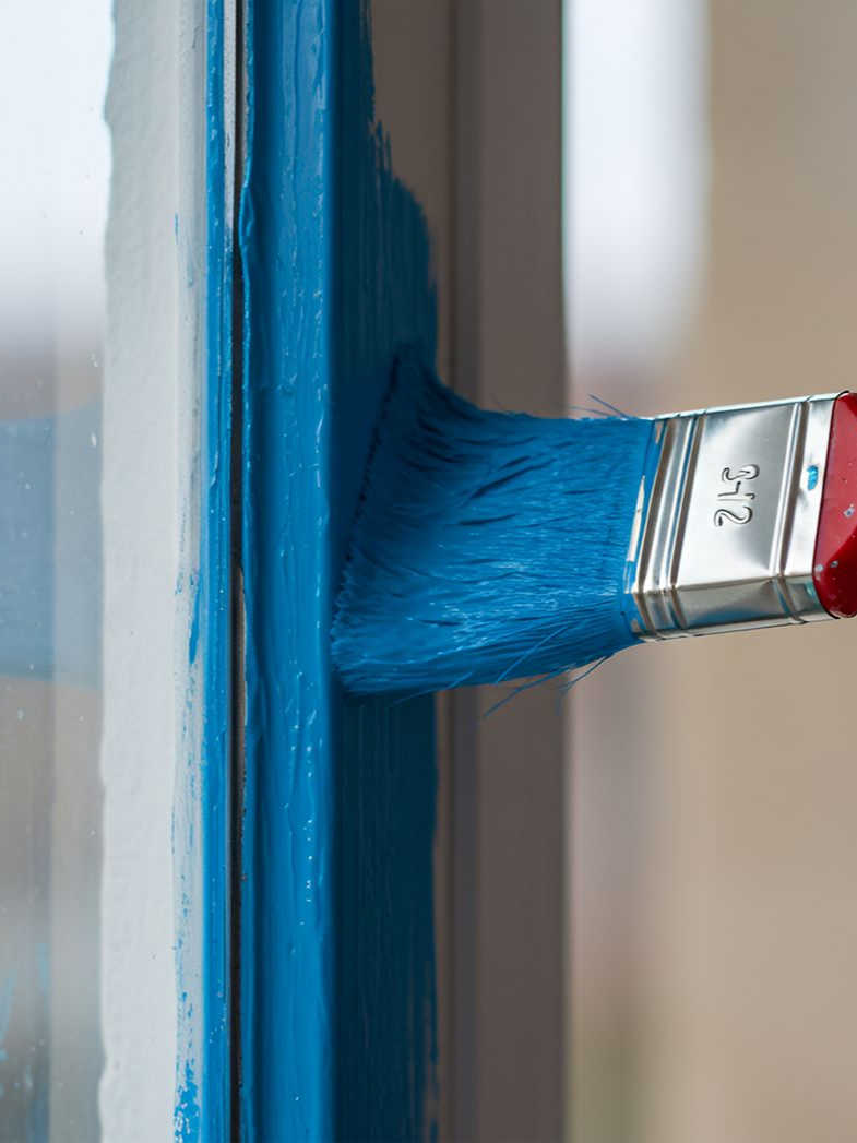 Pinceau bleu peignant un cadre de fenêtre en bleu.