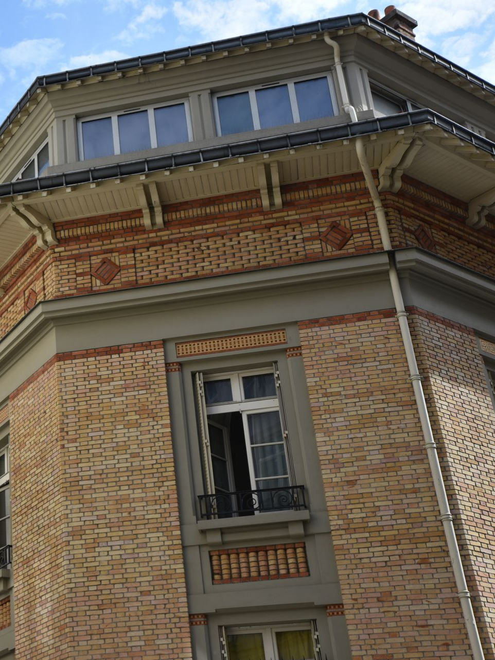 Coin d'un bâtiment en briques avec fenêtres, garnitures et détails décoratifs, sous un ciel bleu.