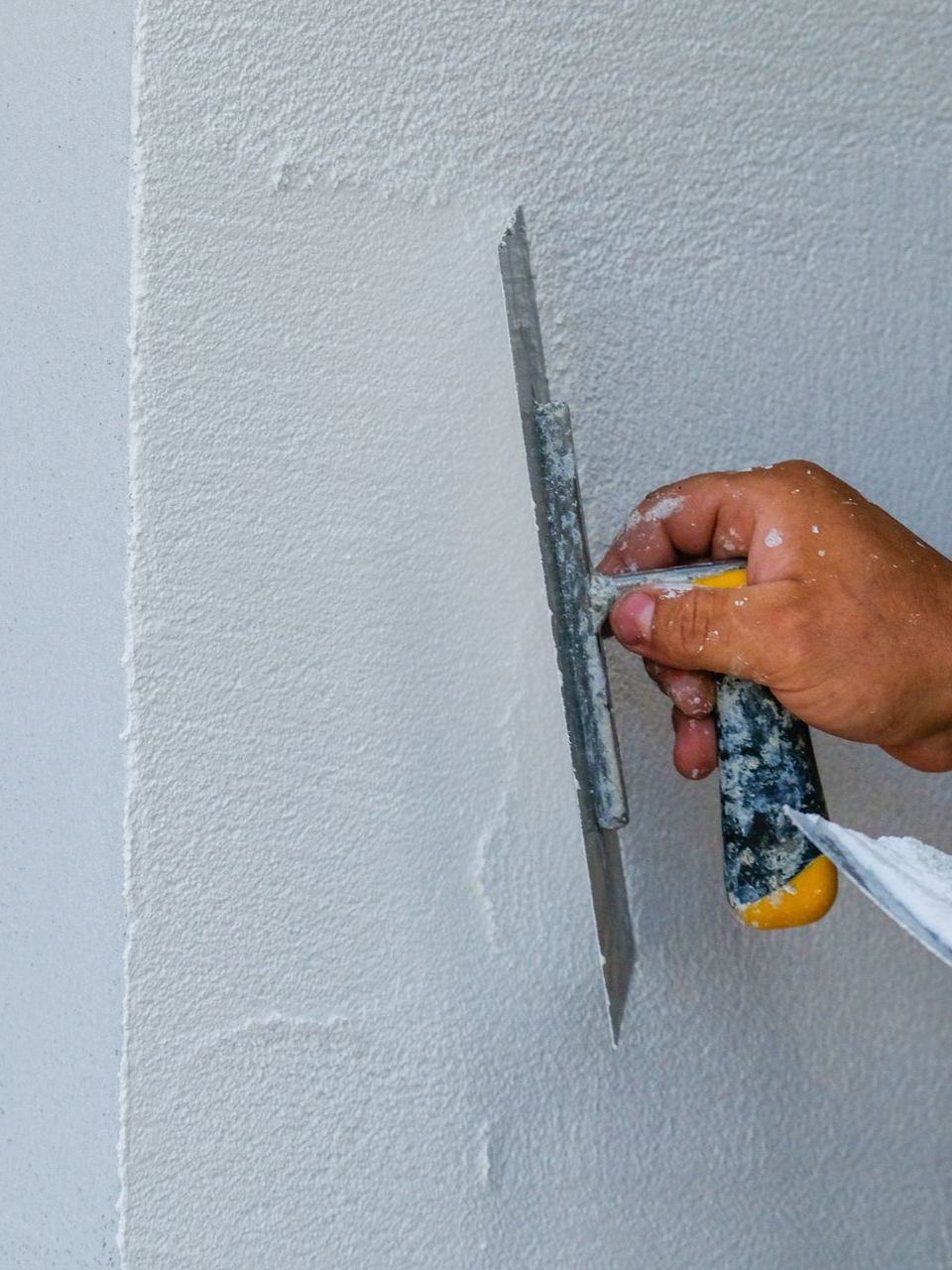 Main utilisant une truelle pour appliquer du plâtre blanc sur un mur, en lissant la surface.
