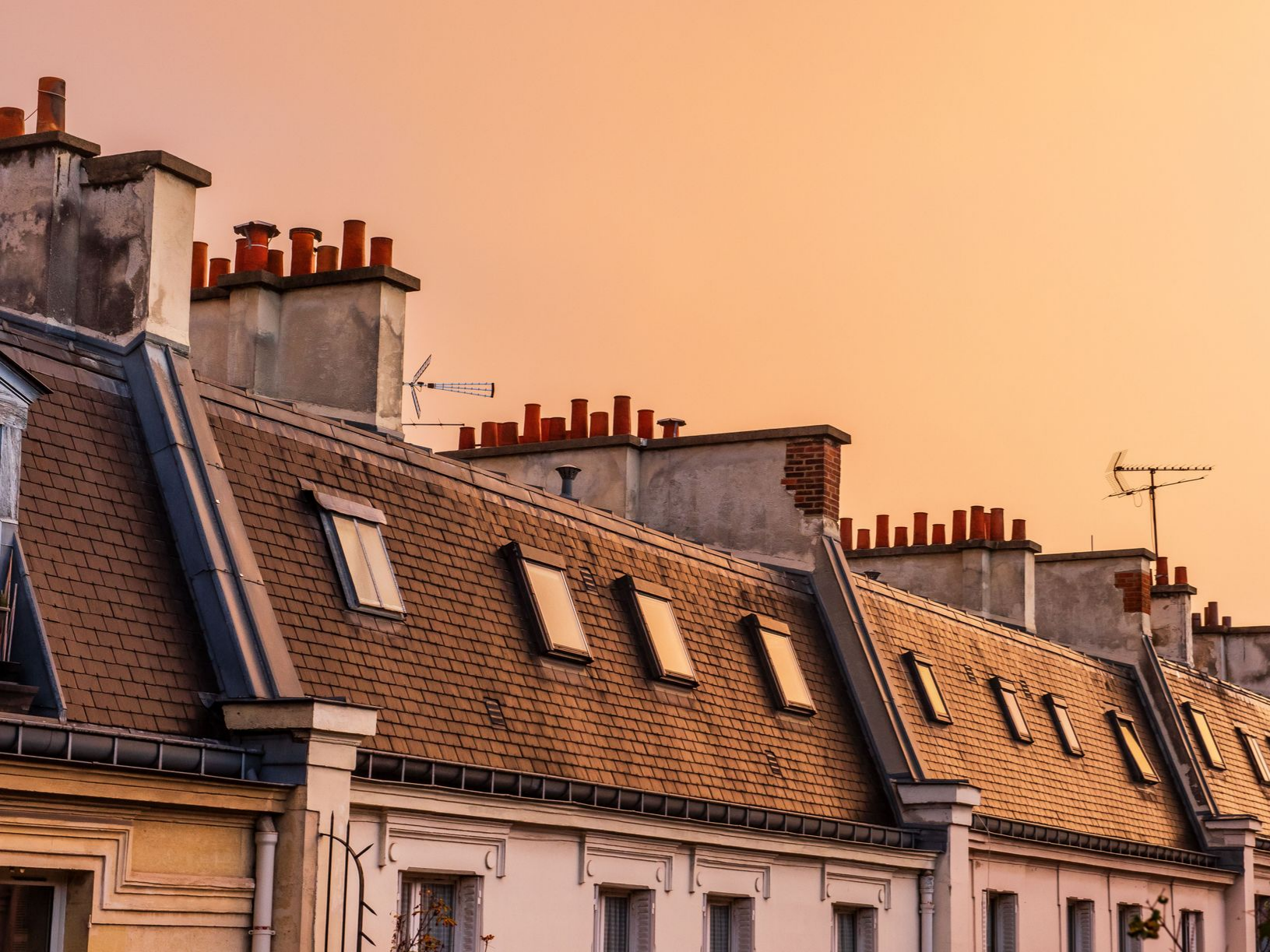 Rangée de toits avec cheminées et lucarnes au coucher du soleil.