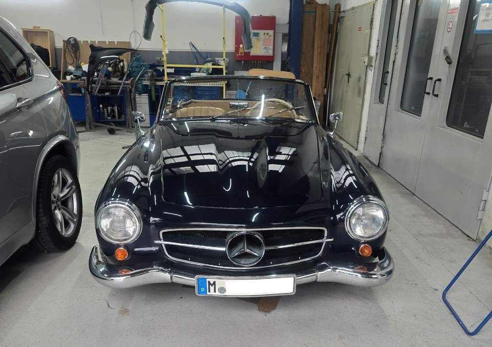 In einer Garage steht ein klassisches, schwarzes Mercedes-Benz Cabriolet neben einem silbernen Auto.