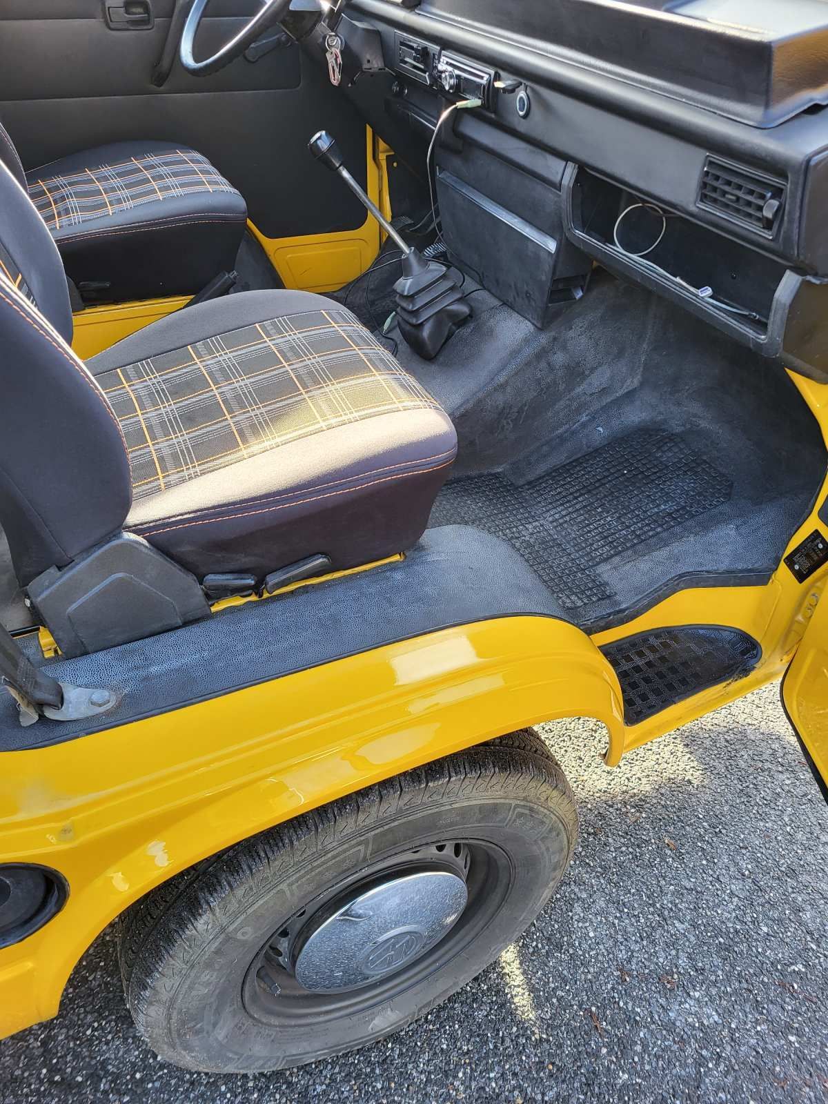 Innenraum eines gelben VW-Transporters, Sitze, Armaturenbrett und Reifen sind sichtbar.