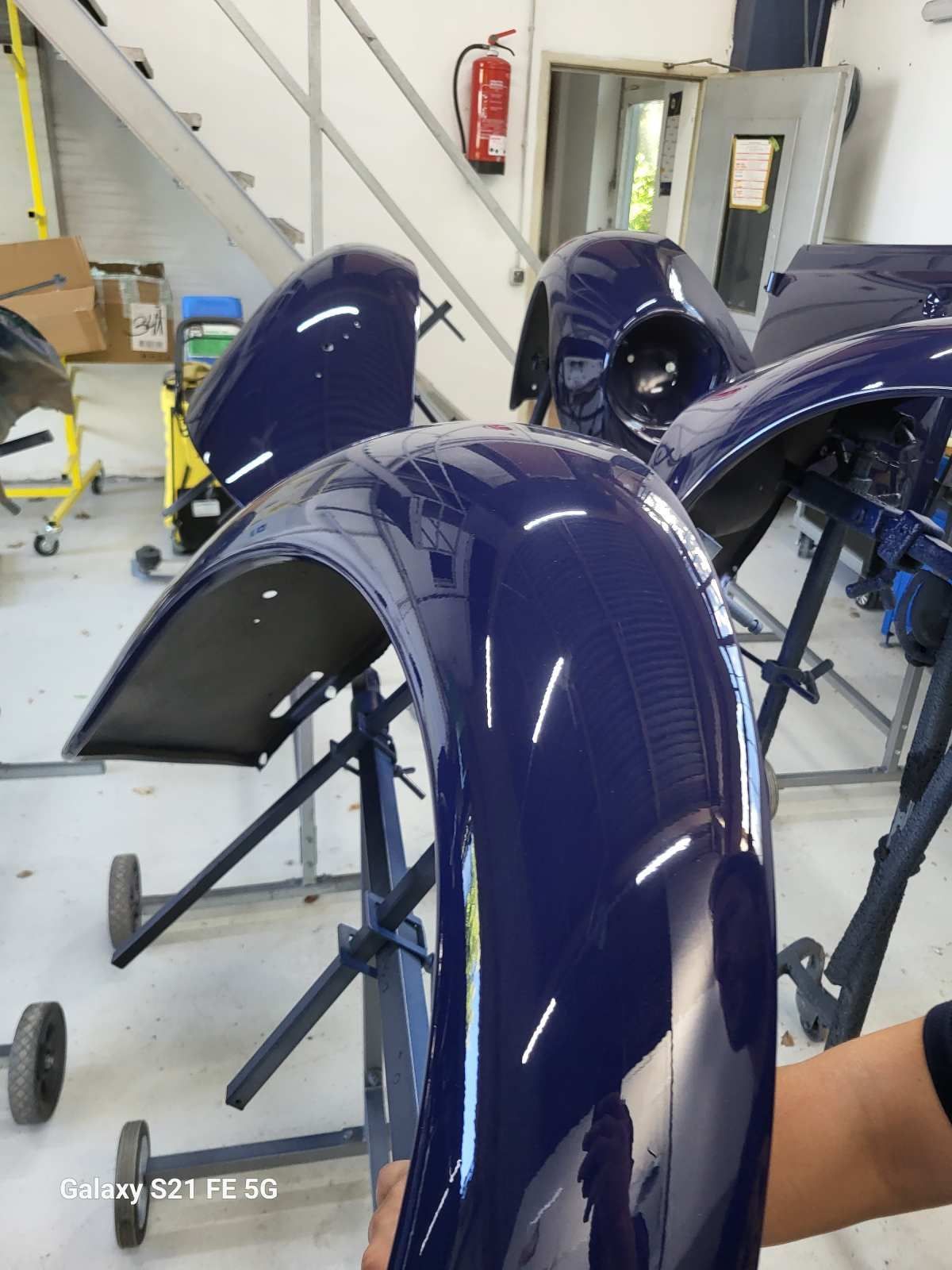 Dunkelblauer Kotflügel in einer Autowerkstatt, andere Teile sichtbar, steht auf Stützen.