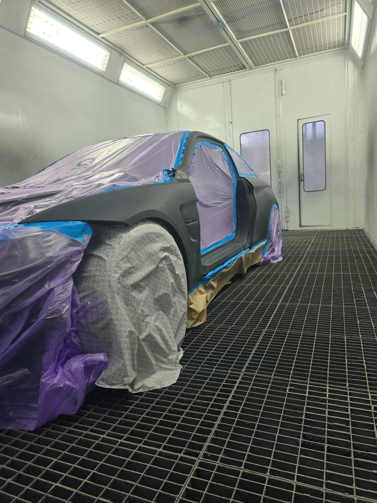 Das Auto steht in der Lackierkabine, ist mit violettem und blauem Klebeband/Abdeckungen abgeklebt und bereit zum Lackieren.
