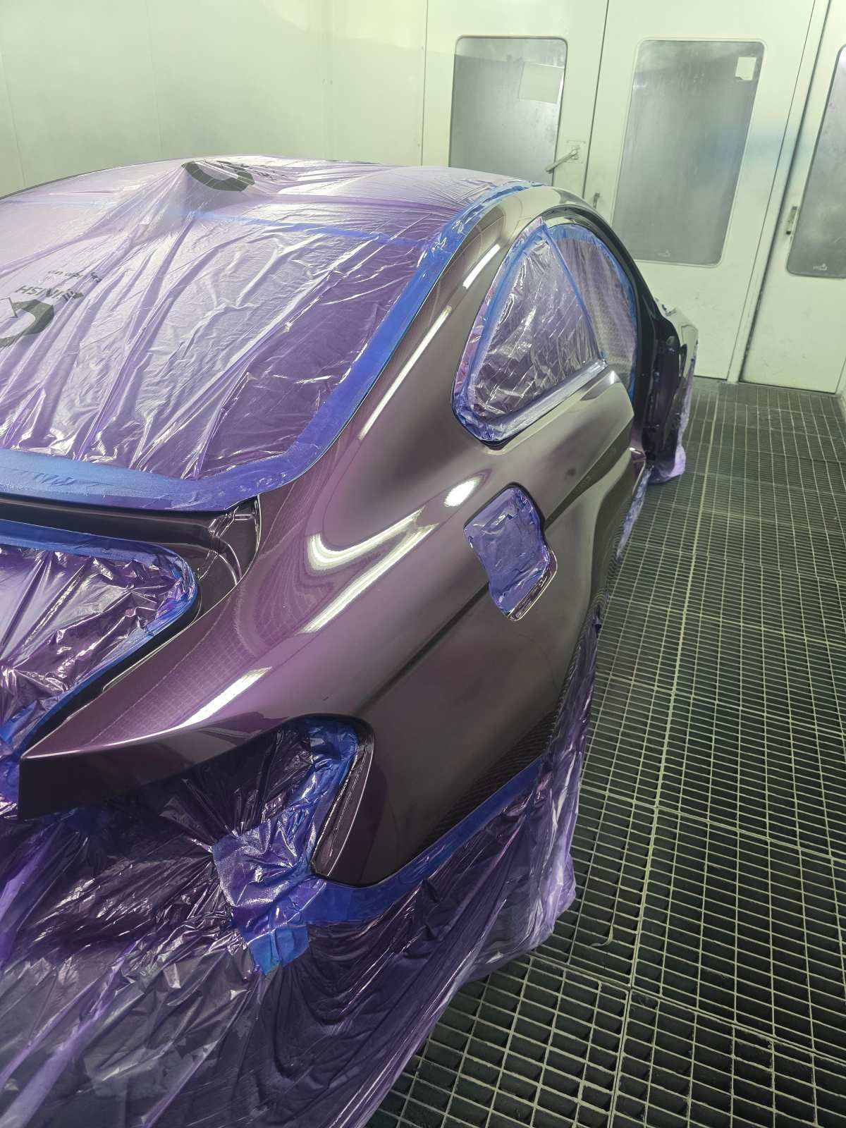 Ein Auto wird in einer Lackierkabine lila lackiert und ist zum Schutz mit Plastikfolie abgedeckt.