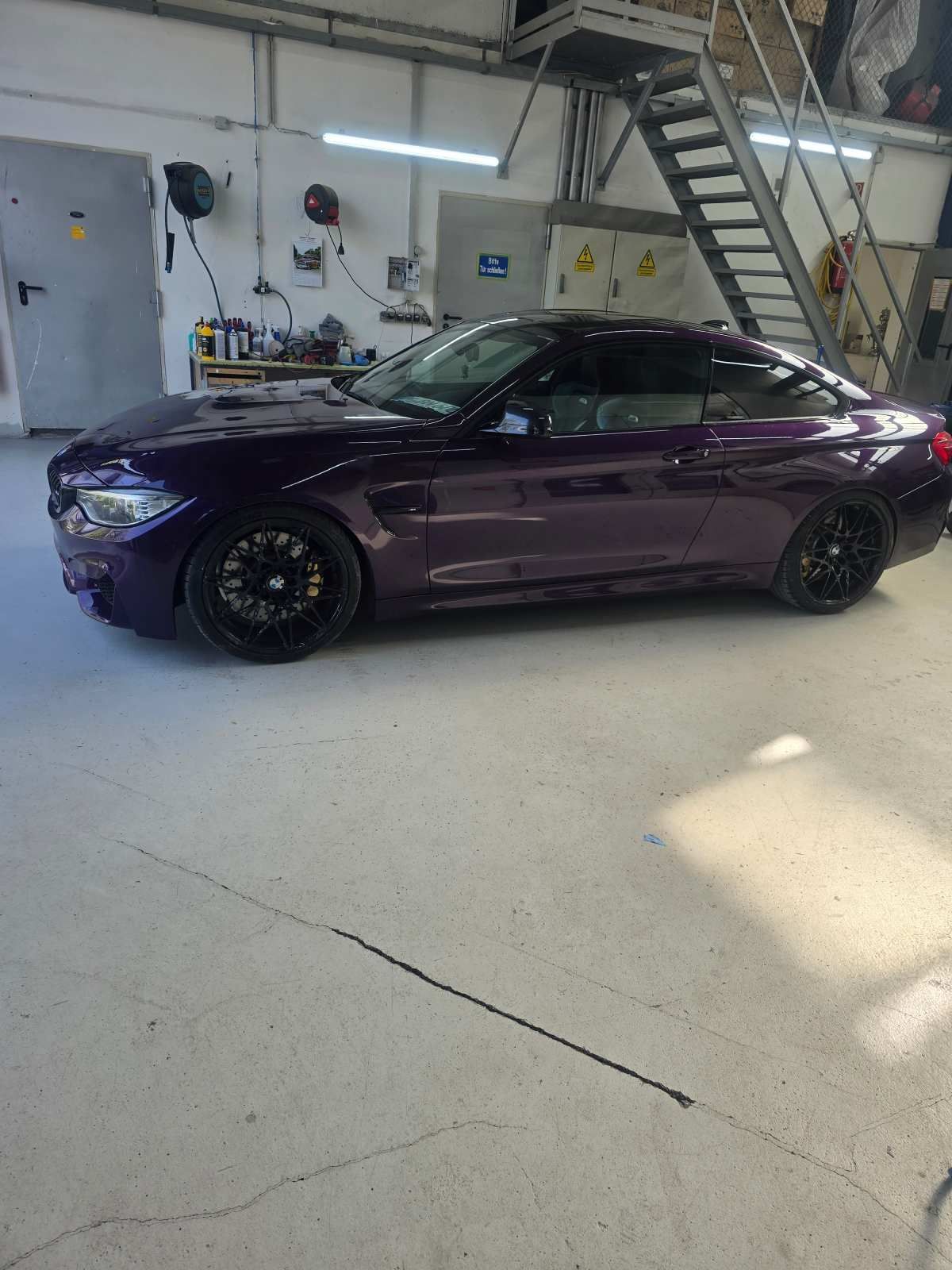 Ein dunkelviolettes Auto mit schwarzen Felgen und einer Leiter im Hintergrund steht in einer Garage.