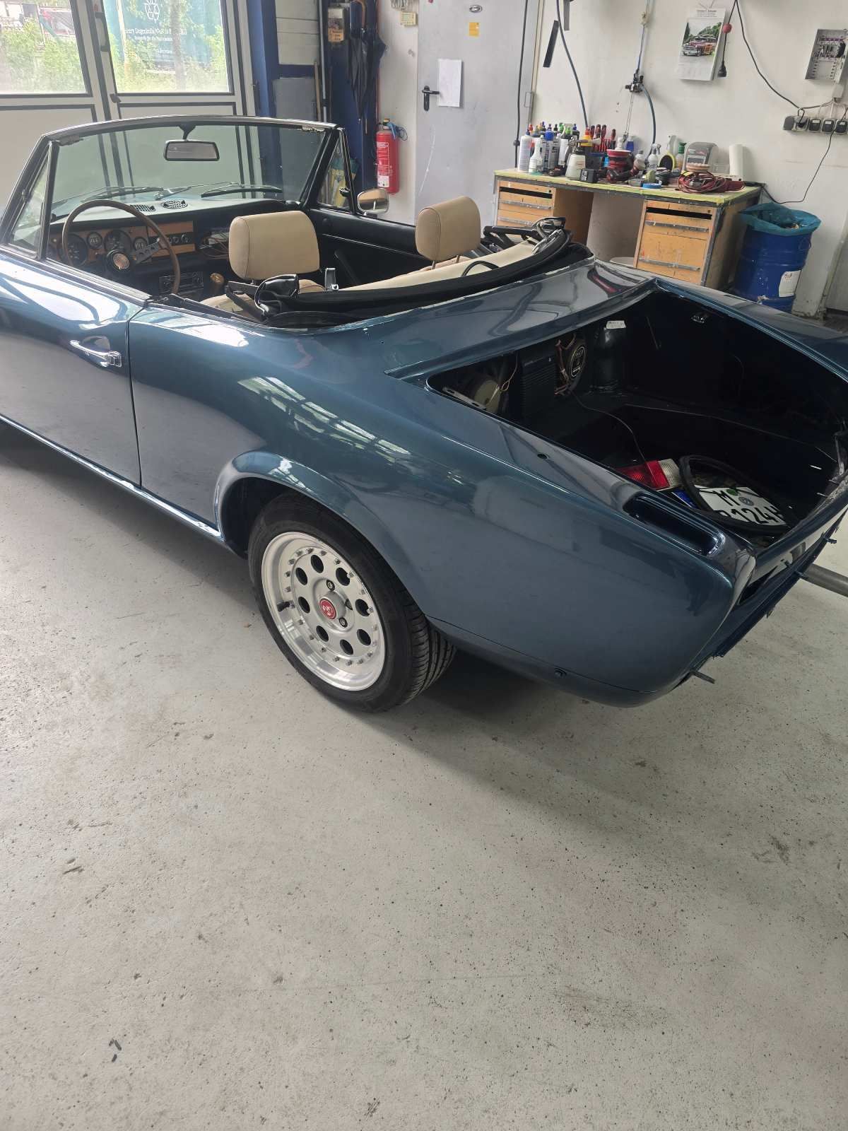 Blaues Cabriolet in einer Werkstatt, Kofferraum geöffnet, beige Innenausstattung.