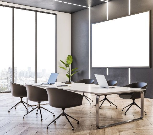 Una sala de conferencias con una mesa, sillas, computadoras portátiles y una pantalla de proyector.