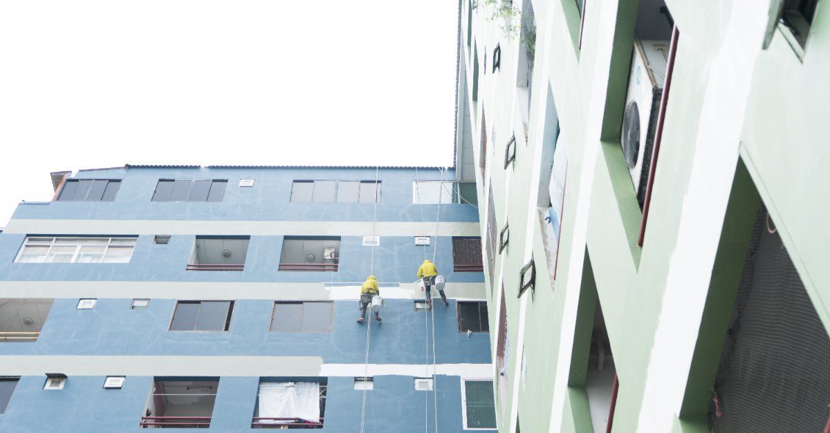 Dos hombres están pintando el costado de un edificio alto.