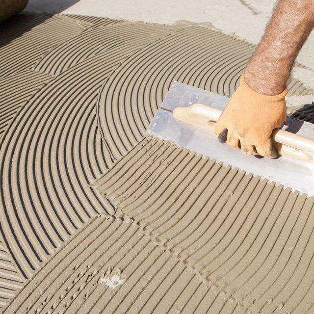 Una persona está extendiendo adhesivo sobre un piso de baldosas.