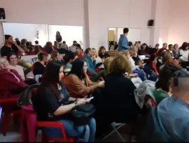 Público sentado en una sala de conferencias, escuchando a un orador situado en la parte delantera.