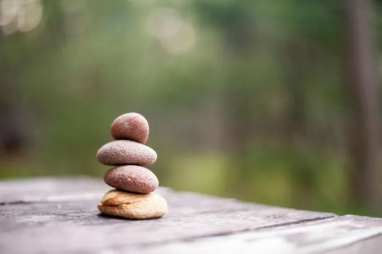 Una pila de cuatro piedras lisas y redondeadas que descansan sobre una superficie de madera con un fondo de bosque verde suave y difuminado.