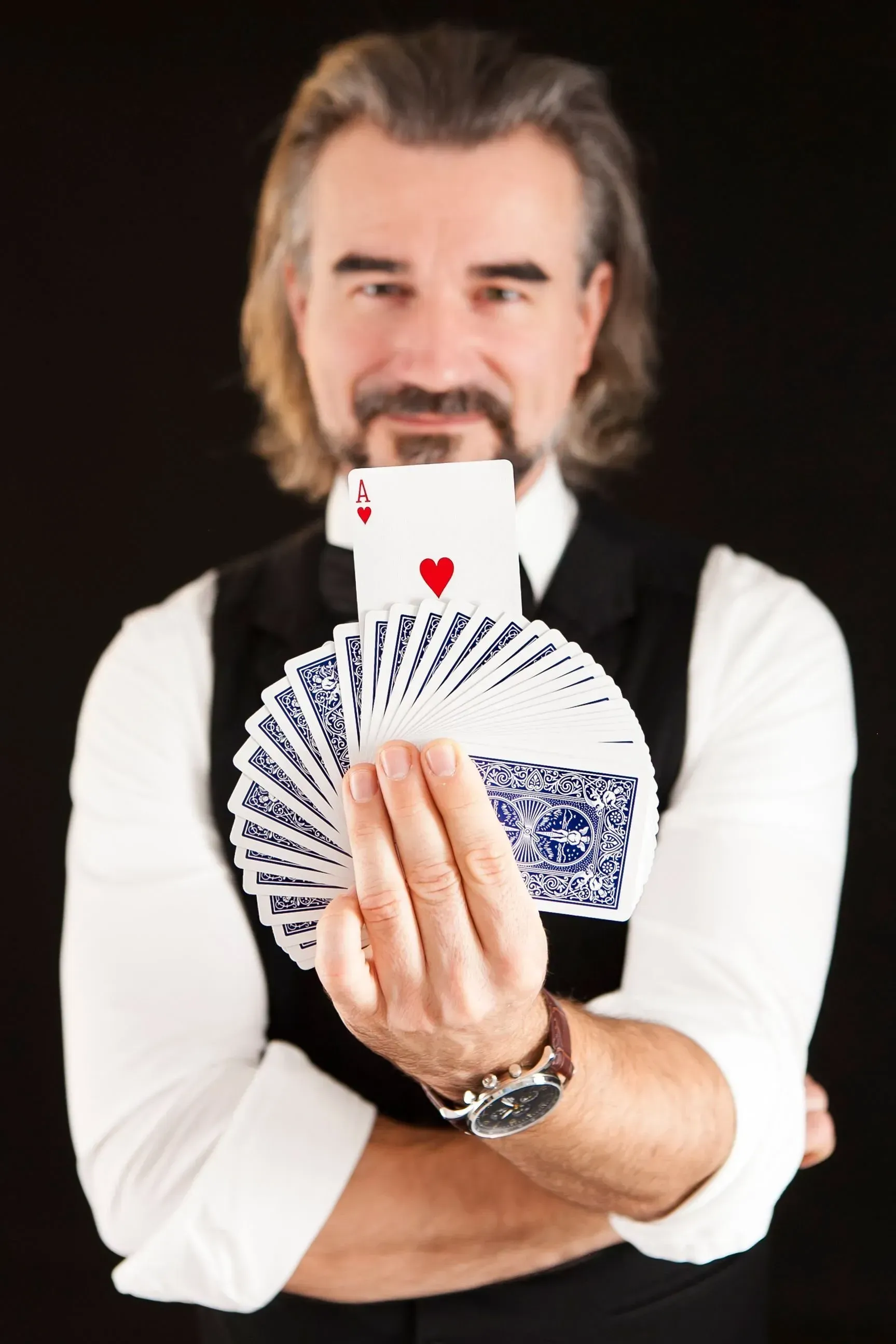 Pascal Thomas im schwarzen Smoking hält ein aufgefächertes Kartenspiel, bei dem das Herz-Ass sichtbar ist