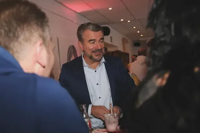 Zauberkünstler Pascal Thomas lächelt auf einer Veranstaltung, hält ein Getränk in der Hand und ist umgeben von Gästen