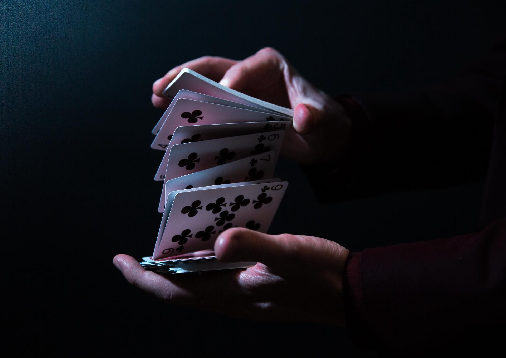 Hände, die im Dämmerlicht Spielkarten auffächern