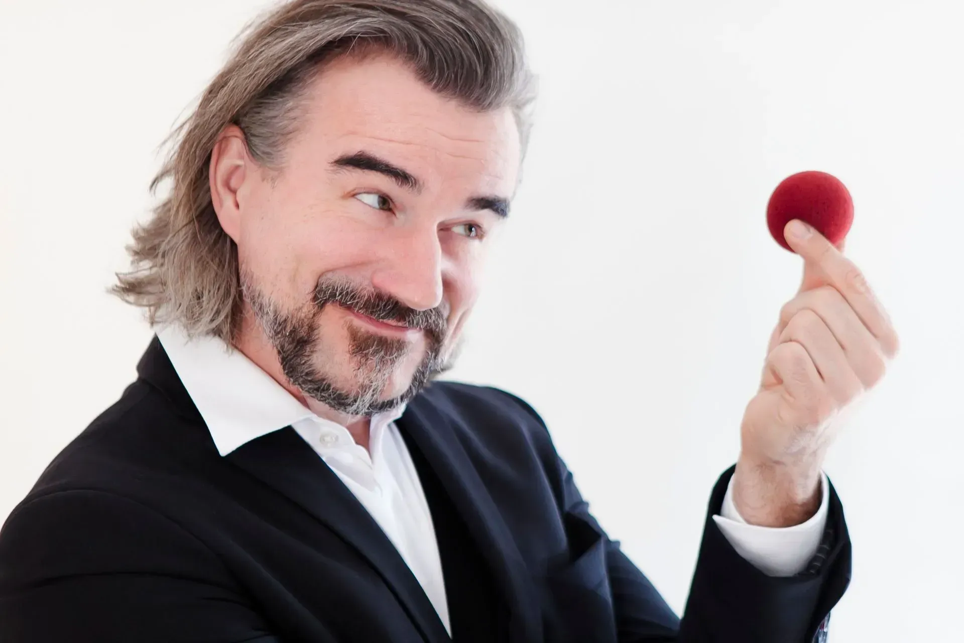 Pascal Thomas im schwarzen Smoking hält einen kleinen roten Ball und grinst dabei