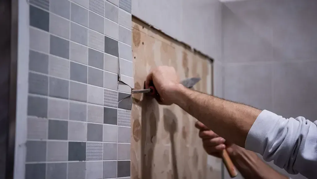 Un hombre está martillando una pared de azulejos con un martillo.